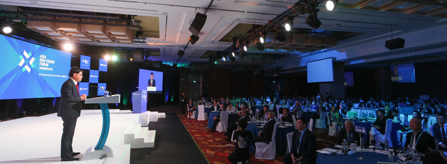 Man at podium on stage for "Asia New Vision Forum" with audience at tables.